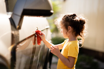 Portrait of a little happy girl in a yellow T-shirt, who helps her dad wash the car outdoor.