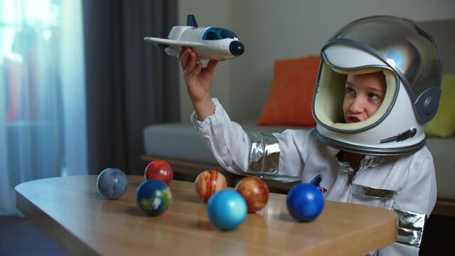 Child plays at home in an astronaut, funny portrait of a little girl 8-9 years old in a toy space suit, a smiling child, launches a space rocket, close-up, a pilot traveling in space. Happy childhood