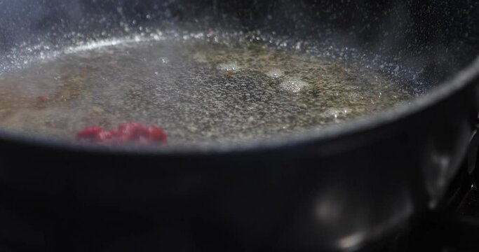 Chef puts tomato paste in frying pan with boiling oil