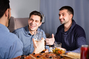 Troubled male friends talking, drinking beer with pizza at home