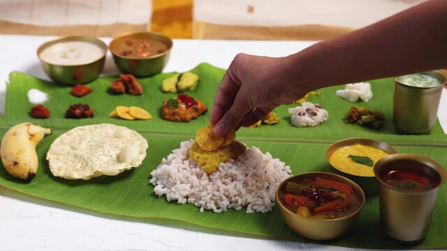 Woman hand serving curry for traditional Onam sadhya 4K footage video rice, Sambar, Rasam,  Avial,  Pappadom Payasam on banana leaf Onam Vishu festival vegetarian food Kerala South India.