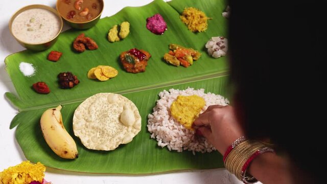 Woman eating traditional Onam sadhya with hand  4K footage video rice, Sambar, Rasam,  Avial,  Pappadom Payasam on banana leaf Onam Vishu festival vegetarian food Kerala South India.