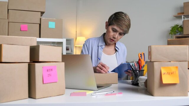 Mature Asian woman entrepreneur, Business owner writing address and delivery detail before shipping product to client
