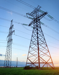 High voltage lines and power pylons in a flat and agricultural landscape on a sunny day with clouds in the blue sky.