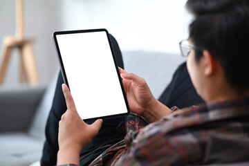 Cropped shot young man sitting on sofa and reading news on digital tablet.