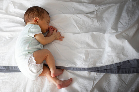 2 months old caucasian newborn baby, sleeping alone in parents bed, lying on side. Background with copy space.