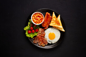 Traditional Full English breakfast, on a black background, fried eggs with fried bacon, sausages, white beans ,cherry tomatoes, horizontal, no people,