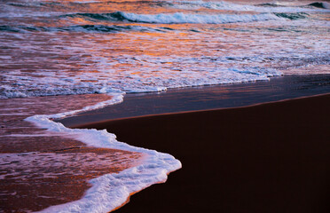 Waves from the Atlantic Ocean reflect the light of the sun as it rises over Whitepark Bay beach on the Antrim Coast, Northern Ireland. 