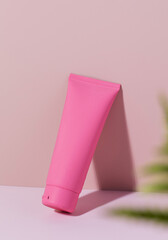 A pink tube with a cosmetic product on a pink background. Mockup cream for face and body.
