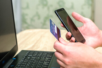 a person in front of a laptop holds a smartphone and a credit card in his hands online business trading concept