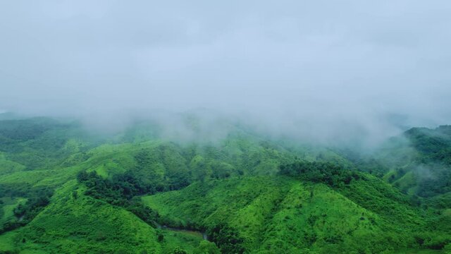 Aerial view drone shot of flowing fog waves on mountain tropical rainforest In the evening,Bird eye view image over the clouds Amazing nature background with clouds and mountain peaks.