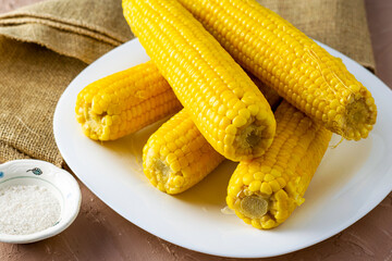 corn cooked on the cob on a white plate, next to a salt shaker with salt
