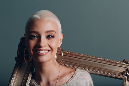 Millenial Young Woman With Short Blonde Hair Holds Gilded Picture Frame In Hands On Her Neck Shoulders Smile Portrait