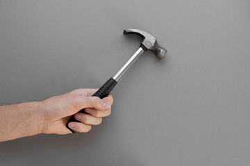 A hand holds a construction hammer on a gray background