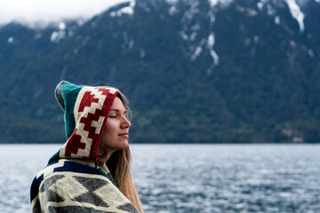 Portrait of a young woman with a relaxed expression wearing a colorful poncho in the rain on her...