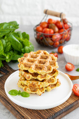 Homemade zucchini cheese waffles with sour cream and fresh basil on a plate on a gray concrete background. Vegetarian dish. Copy space.