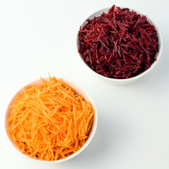 Fototapeta premium Fresh grated carrot and beet in white bowls, on a white plate. A set of vegetables for borscht. Selective focus. Side and top view.