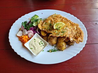 Home-style fish fillets with potatoes and fresh salad on a plate are prepared for lunch