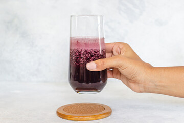 Mano de chica sujetando vaso de cristal con granada de remolacha morada fresco fondo blanco, composición amplia. Detox, dietética, pérdida de peso, concepto de estilo de vida saludable