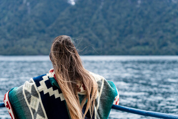 Young woman wearing a colorful poncho looking towards the snow-capped mountains on the way to peulla