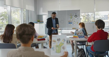 Back view of diverse teen kids sitting at desk having ecology lesson with mature teacher