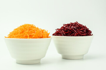 Grated carrot and grated beet in a white bowl. Set of vegetables for cooking lunch. Selective focus. Side view.