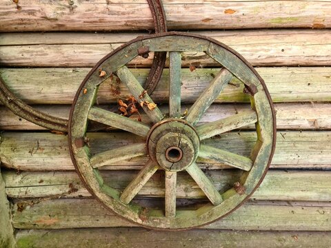 Wooden wheel from an old cart is fixed on the wall of a utility shed