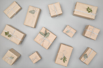 Pattern made of small gift boxes wrapped in craft paper with dried eucalyptus leaves on solid gray...