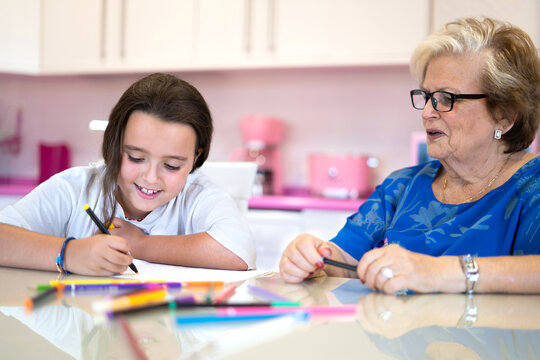 Positive girl drawing on paper while sitting with grandmother at home