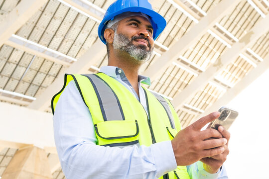Ethnic supervisor in hardhat with smartphone against solar power station