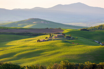 Fototapeta na wymiar Sunlit field at dawn with a farm in Tuscany, Italy