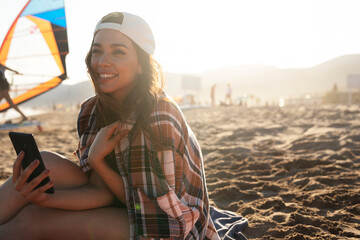 Portrait of beautiful female surfer with her surfboard. Young woman having video call while relaxing at the beach.