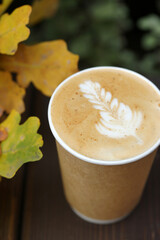 Cappuccino in a paper cup on a wooden table