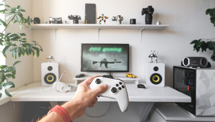 Close-up of male hands holding white wireless gamepad against white computer dream desk.
