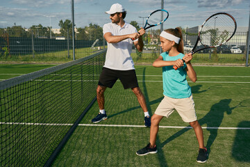 Father is a tennis coach for his daughter. Female child is playing in tandem with her daddy in doubles tennis