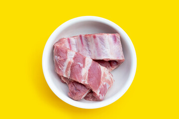 Raw pork ribs in white bowl on yellow background.