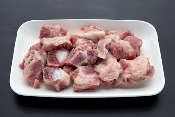Raw pork ribs in white plate on dark background.