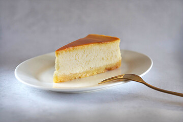 A piece of caramel cheesecake on a saucer on the table with a gold fork next to it.