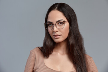 Fototapeta premium Confident young business woman 35-45 years old, brunette in stylish formal clothes and glasses, gray background, close-up. Business and career success concept.