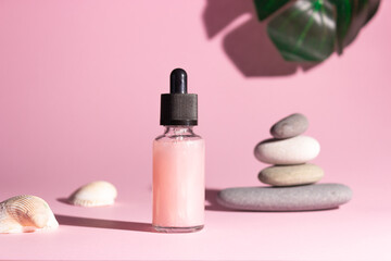 Obraz na płótnie Canvas Cosmetic product in a glass bottle with a pipette on a pink background. Smooth stones nearby. The concept of skin care, cosmetology.