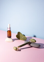 Cosmetic product in a glass bottle with a pipette and gua sha e scraper and roller. Smooth stones nearby. The concept of skin care, cosmetology.