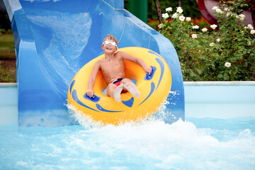 happy an 8 year old boy is riding in the water Park on inflatable circles on water slides with...