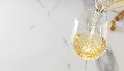 Closeup of of wine glass and process of pouring white wine, corkscrew and cork on the white marble...