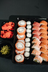 Japanese food concept. Catering, various kinds of sushi on plate. Placed on stone black background in plastic delivery box. Sushi roll (Philadelphia) with salmon, smoked eel, avocado, cream cheese.