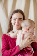 A young mother with long dark hair in a burgundy dress with a baby in her arms on a light background. Healthy lifestyle. Happy motherhood 