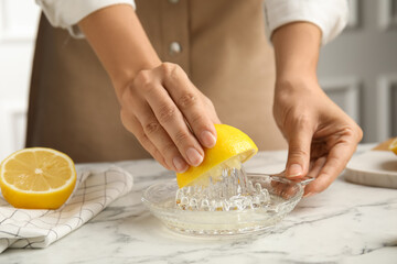 Obraz na płótnie Canvas Woman squeezing lemon juice at white marble table, closeup