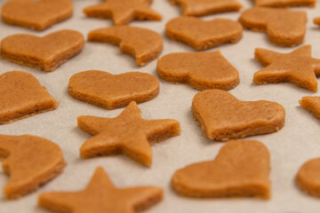 Close up of raw Speculaas cookies on a baking paper, ready for baking. Dough is in the shapes of heart, star and crescent moon.