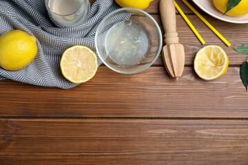 Citrus reamer, juice and fresh lemons on wooden table, flat lay. Space for text