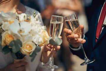 the bride and groom hold champagne glasses, a wedding bouquet