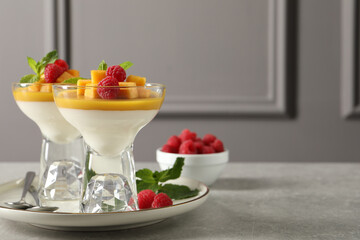 Delicious panna cotta with mango and raspberries on grey table. Space for text